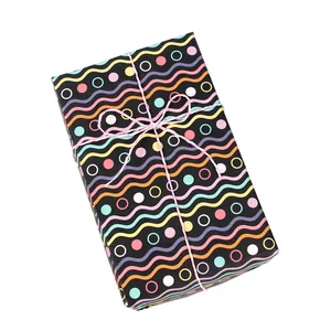 Papel de regalo negro con diseño de ondas y puntos coloridos, atado con un lazo rosa