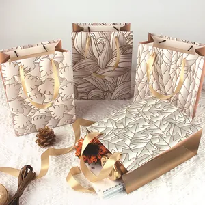 Elegante Geschenktüten aus weißem Karton mit goldenen Glitzerblattmustern und Band