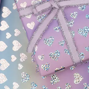 Primo piano di carta regalo olografica viola con cuori glitterati e un nastro argentato lucido.