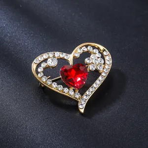 Detailed macro view of a gold-tone heart brooch with red faceted crystal and rhinestones