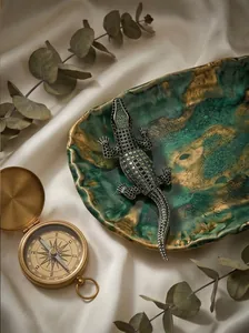 Close-up detail of sparkling crocodile brooch with green crystals on a marble plate