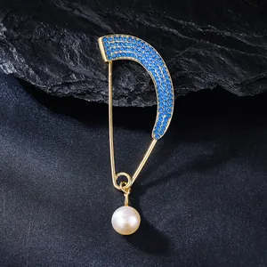 Close-up of gold curved brooch with blue rhinestones and pearl pendant on slate.