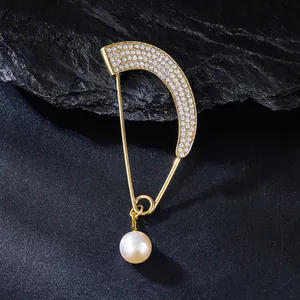 Detailed view of an elegant curved gold brooch featuring rhinestones and a hanging pearl