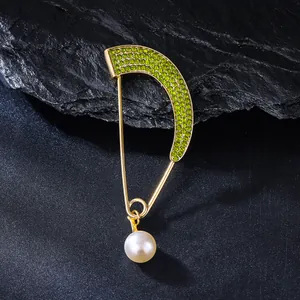 Macro detail of gold arc brooch with green rhinestones and pearl pendant.