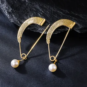 Detail macro view of gold-tone curved safety pin brooch with an elegant white pearl drop