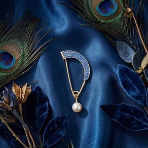 Elegant gold curved brooch with blue rhinestones and pearl drop on silk background