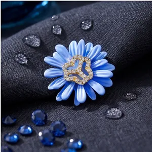 Elegante broche de margarita azul claro con centro de cristal sobre fondo de tela gris oscuro