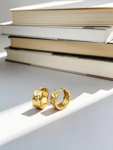 Primo piano di orecchini a cerchio placcati oro con trama a ghiaccio tritato su bianco
