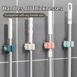 Wall-mounted mop and broom holders in various colors shown holding poles on grey tile wall