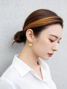 Vista de perfil de una modelo asiática con pendientes de plata dorada con textura tallada.