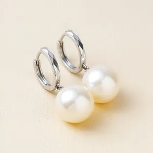 Primer plano de pendientes de aro de plata con grandes gotas de perlas blancas.