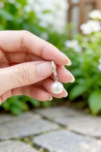 Primer plano de un pendiente de aro de plata S925 con perla colgante y grabado detallado.
