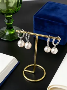 Primer plano de pendientes de aro de plata S925 con elegantes perlas colgantes en soporte