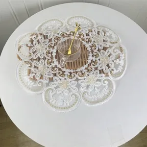 Detail of a 42cm round white floral embroidered lace placemat on a rustic wooden tray