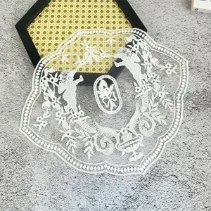 Detail view of a white embroidered lace patch featuring vintage cherub and floral patterns