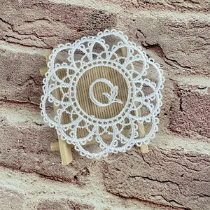 Detailed view of a white mesh lace coaster with embroidered letter Q