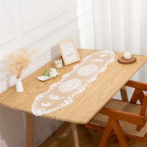 Detail view of an elegant white hollow lace table runner on a rustic wooden dining table