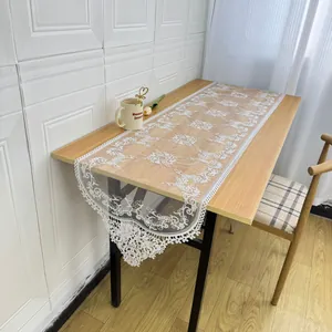 Elegant white lace table runner with floral embroidery displayed on a wooden table.