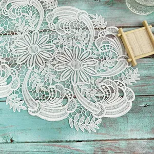 Close-up detail of white water-soluble lace floral placemat on teal wooden background