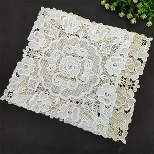 Detailed embroidery texture of the square white and beige lace placemat on dark background.