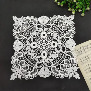 Macro detail of white square lace doily with elegant floral embroidery patterns.