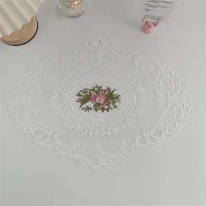 Detailansicht eines eleganten, ovalen Tischsets aus weißer Spitze mit Rosenstickerei
