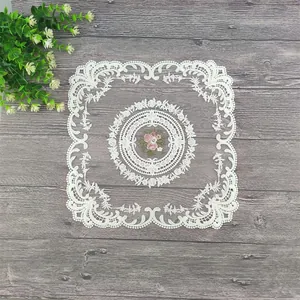 Detailaufnahme eines weißen quadratischen Spitzentischsets mit eleganter Blumenstickerei