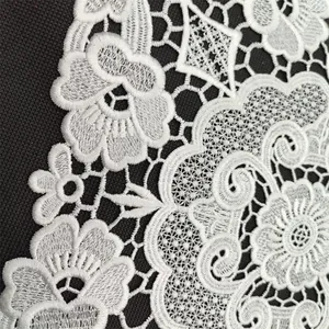 Intricate white floral lace embroidery detail on dark textured background surface