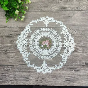Nahaufnahme eines weißen runden Spitzen-Platzsets mit Blumenstickerei auf rustikalem Holztisch
