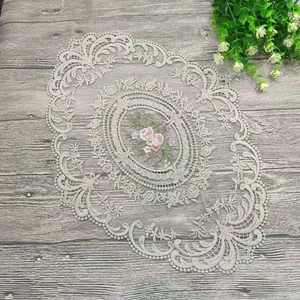 Nahaufnahme eines eleganten, ovalen, bestickten Spitzendeckchens mit rosa Blumen