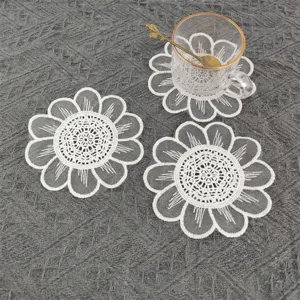 Close-up of white embroidered lace coaster with floral patterns on grey fabric.