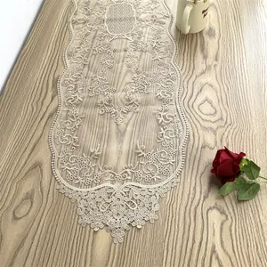Eleganter beiger Tischläufer aus Spitze mit Blumenstickerei auf einer Holzoberfläche.