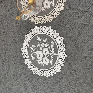 Exquisite detail of white floral embroidery on a round mesh lace coaster on gray cloth.