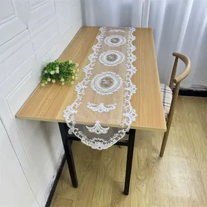 Detail of an elegant white lace table runner with floral embroidery on a wooden table.