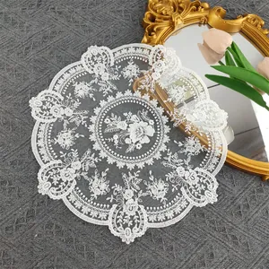 Detail view of white circular embroidered floral lace doily with scalloped edges.