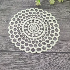 Primer plano del posavasos de encaje bordado blanco sobre fondo de madera oscura.