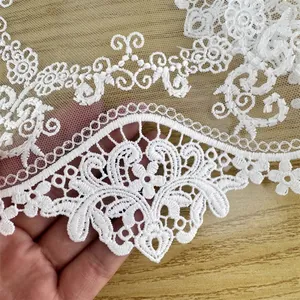 Detailed close-up of white embroidered lace tablecloth with delicate floral fringe