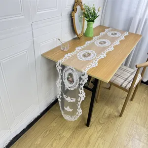 Detail showing the elegant white lace embroidered table runner with floral pattern on wood desk.