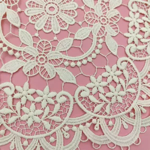 Close-up detail of white hollow-out embroidered floral lace placemat on pink background