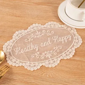 Close-up of white lace coaster with 'Healthy and Happy' embroidery on wooden surface