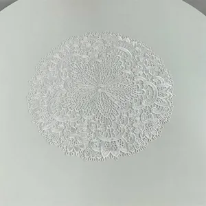 Macro detail of white circular lace doily featuring intricate floral embroidery patterns