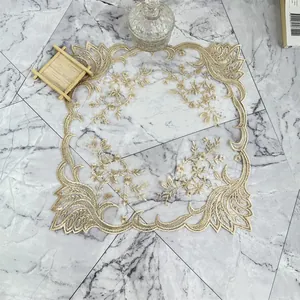 Mantel individual europeo de malla bordada con flores doradas y bordes festoneados.