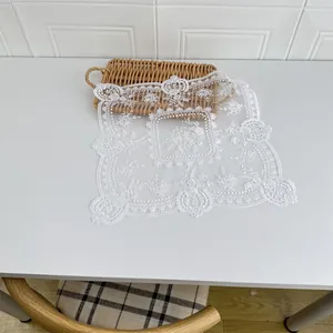 Detailansicht eines weißen Blumen-Spitzendeckchens mit eleganter Stickerei auf Tisch.
