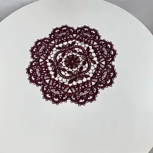 Macro detail of dark burgundy embroidered lace placemat on elegant white surface