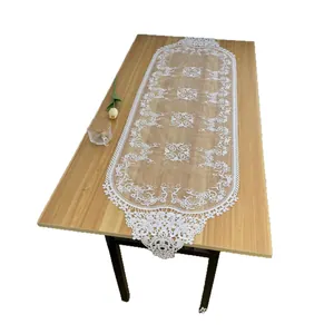 Elegant white lace table runner with hollow floral embroidery on wooden table