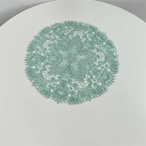 Detailed overhead view of a mint green embroidered lace placemat on a white table.
