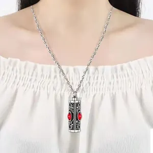 Close-up of silver cylinder cremation urn necklace with red birthstone on model