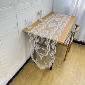 Elegant white lace table runner with intricate floral embroidery shown on a wooden dining table