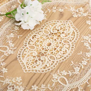 Detailed macro view of intricate hollow-out lace embroidery on a beige table runner.