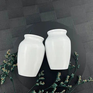 Detail of two white ceramic cremation urns for human or pet ashes on black background.